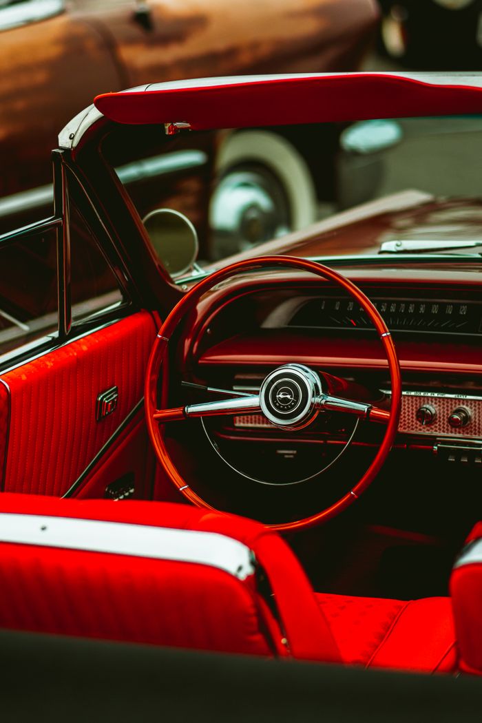 Close-up of a vintage red convertible car interior featuring a classic steering wheel and dashboard.